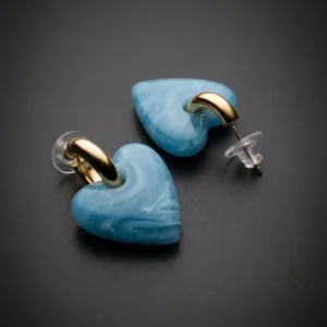 Aretes Milagro Celeste de Arcano: corazones en resina veteada celeste colgados de argollas doradas
