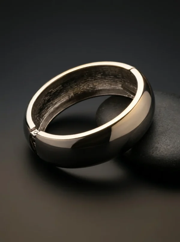 Brazalete Eclipse Plata de Arcano: brazalete rígido de domo con cierre de bisagra, apoyado sobre una piedra negra